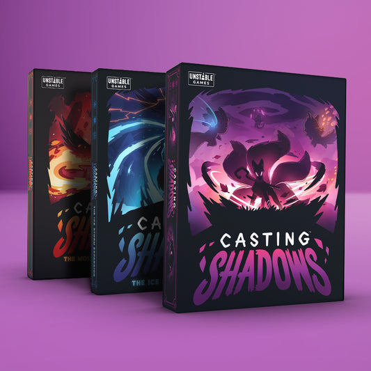 Three Unstable Games board boxes rest on a pink backdrop, with 